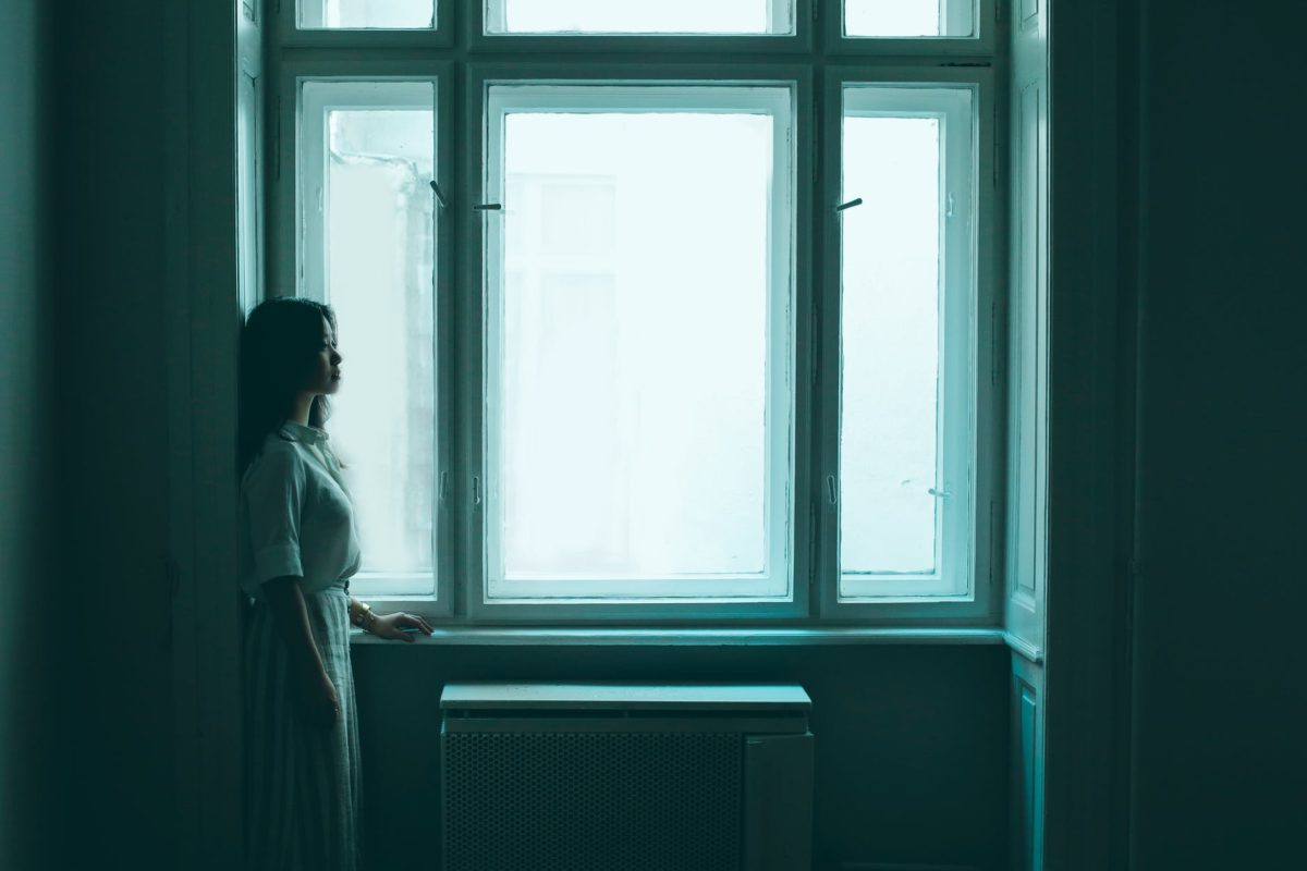depressed asian female standing near window